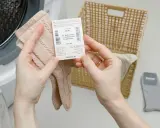 Ręce trzymają metkę z informacją, w czym prać wełnę merino, obok kosza i pralki.