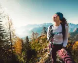 Kobieta w sportowym outfit w górach, z kijkami trekkingowymi, podziwia jesienny krajobraz.