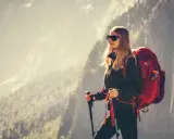 Kobieta w stroju w góry damski, z plecakiem i kijkami trekkingowymi, podziwia górski krajobraz.