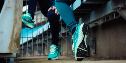 Dwie osoby w turkusowych butach sportowych siedzą na schodach. Dowiedz się, jak zdezynfekować buty, by były świeże i czyste.