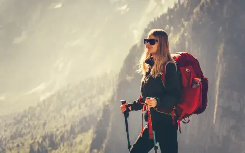 Kobieta w stroju w góry damski, z plecakiem i kijkami trekkingowymi, podziwia górski krajobraz.