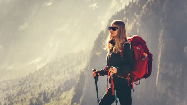 Kobieta w stroju w góry damski, z plecakiem i kijkami trekkingowymi, podziwia górski krajobraz.
